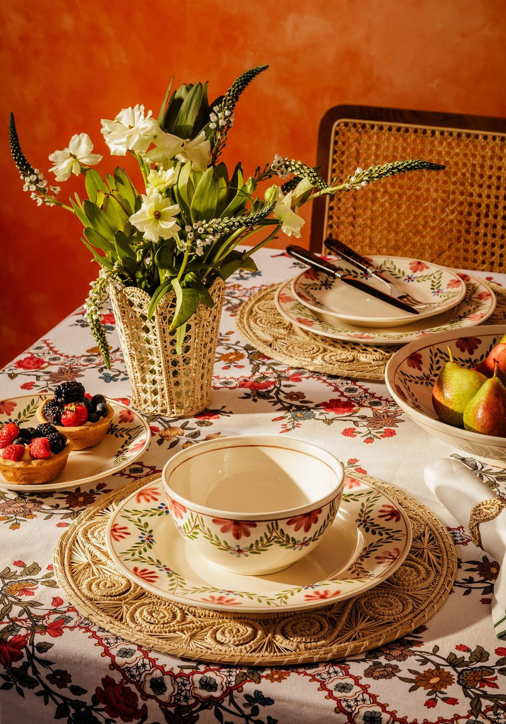 Dining table setting with floral arrangement, plates, and cutlery against an orange wall.