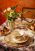 Dining table setting with floral arrangement, plates, and cutlery against an orange wall.