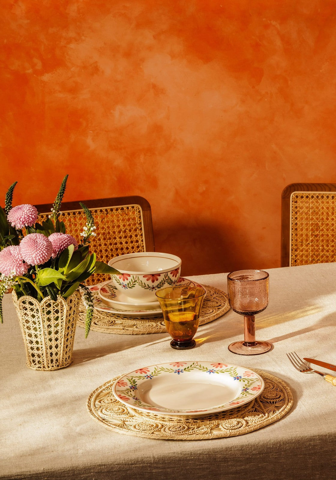Dining table setting with floral arrangement, plates, and glasses against an orange wall.