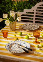 Outdoor table setting with yellow striped tablecloth, white tulips, and blue and white plates.