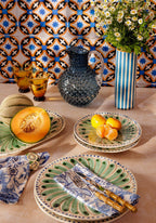 Decorative table setting with ceramic plates, a pitcher, and fruit against a patterned tile wall.
