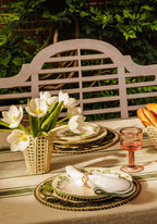 Dining table setting with white tulips, gold and green plates, and a bench in the background.