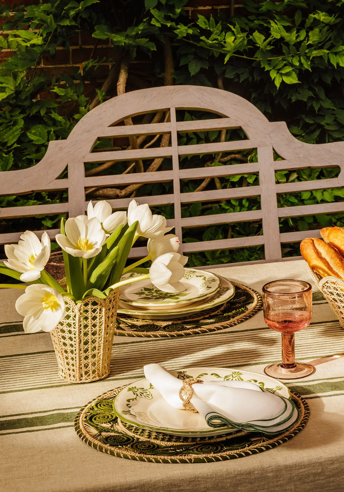 Dining table setting with white tulips, gold and green plates, and a bench in the background.