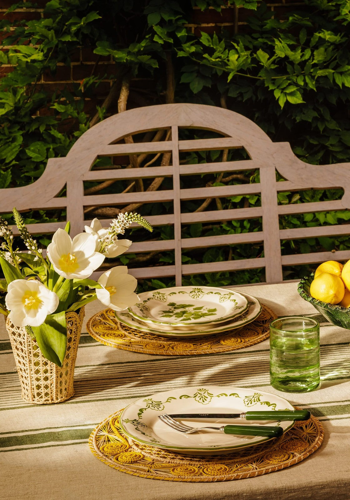 Outdoor table setting with plates, glasses, and flowers on a wooden bench.
