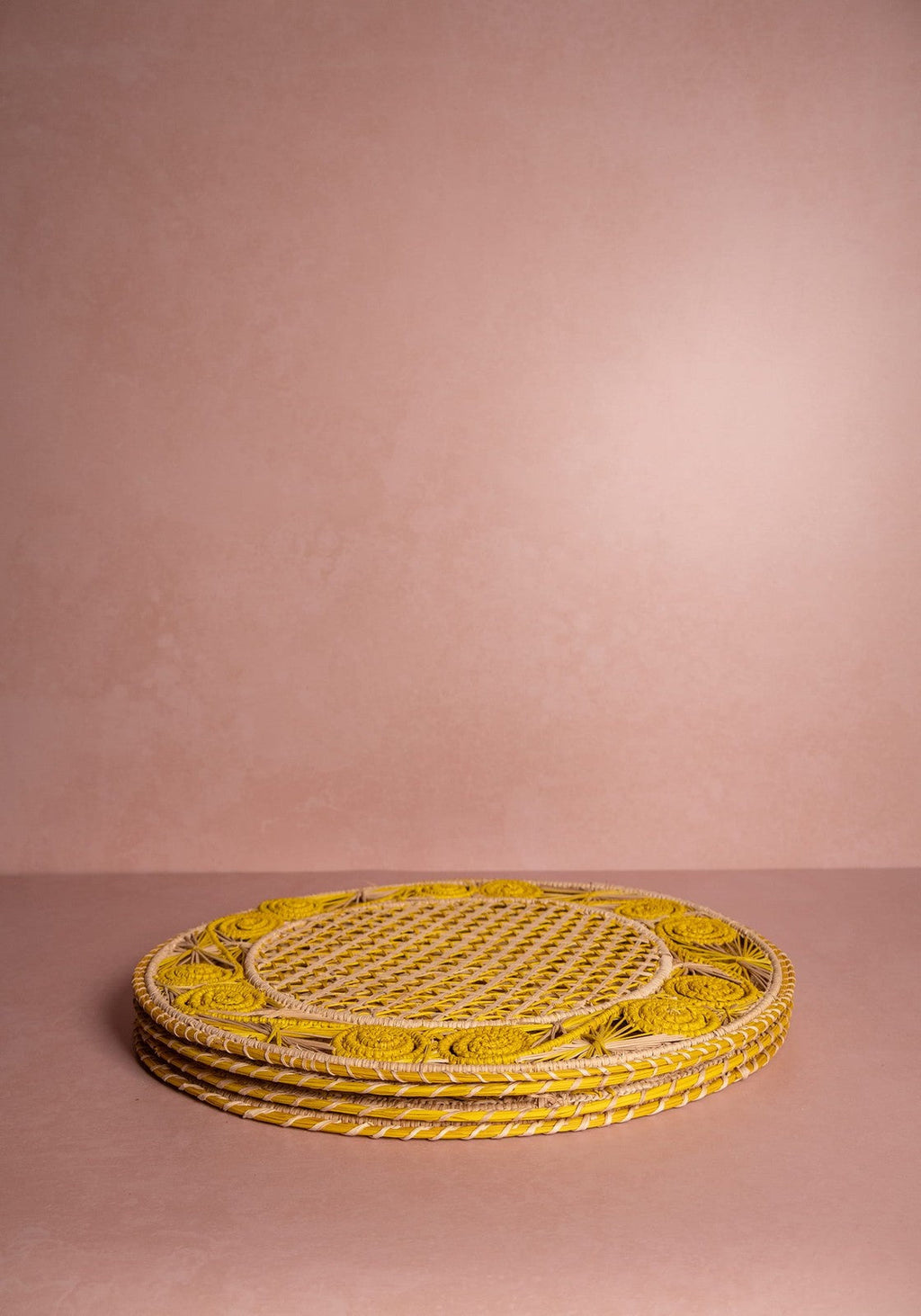 Stack of yellow woven placemats on a pink background
