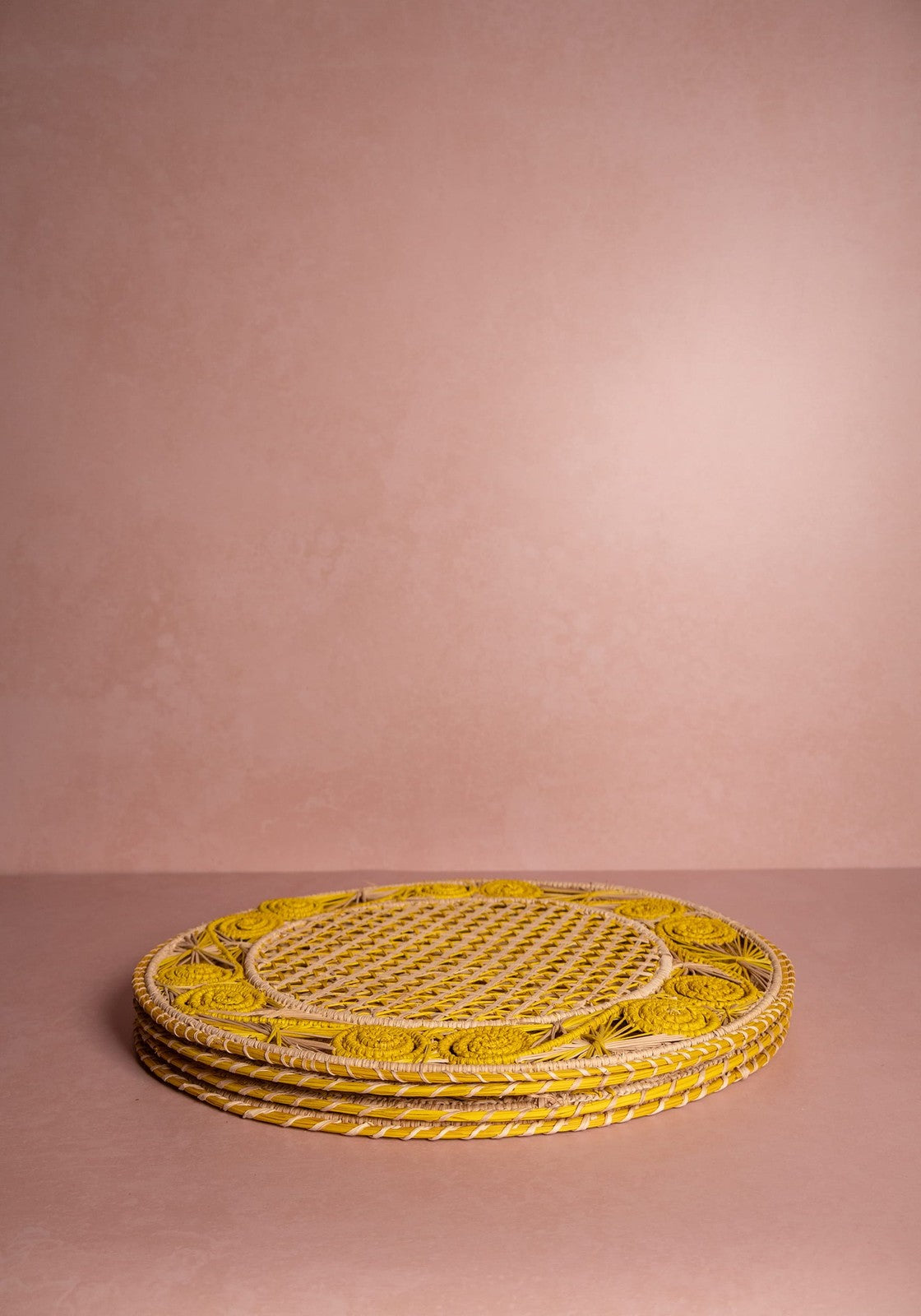 Stack of yellow woven placemats on a pink background