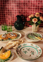 Table setting with pancakes, fruit, and decorative plates against a tiled wall.