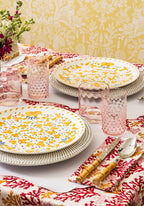 Dining table setting with floral plates, pink glasses, and a red and white patterned tablecloth.
