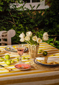 Outdoor table setting with white tulips in a vase, colorful plates, and green apples on a striped tablecloth.
