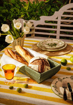 Outdoor table setting with bread, plates, and a vase of flowers on a yellow and white striped tablecloth.